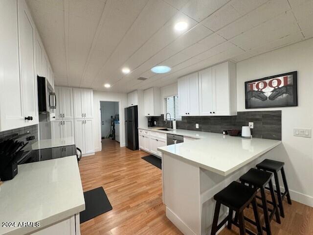 kitchen featuring white cabinets, light wood-type flooring, a breakfast bar area, stainless steel appliances, and kitchen peninsula