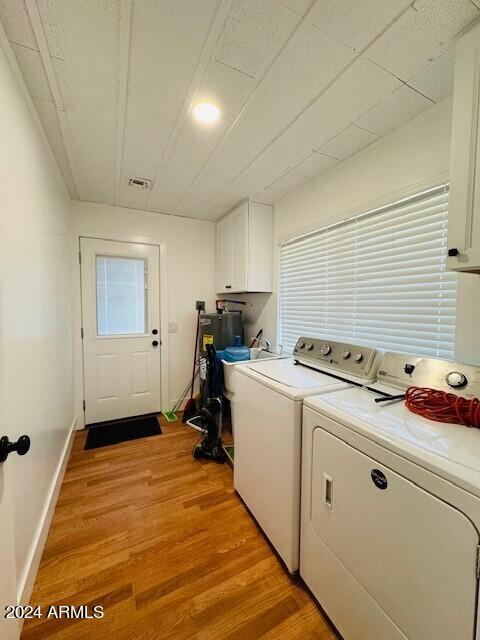 washroom with light hardwood / wood-style flooring, cabinets, and washer and dryer