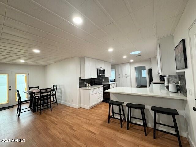 kitchen featuring backsplash, light hardwood / wood-style flooring, white cabinetry, and black range with electric cooktop