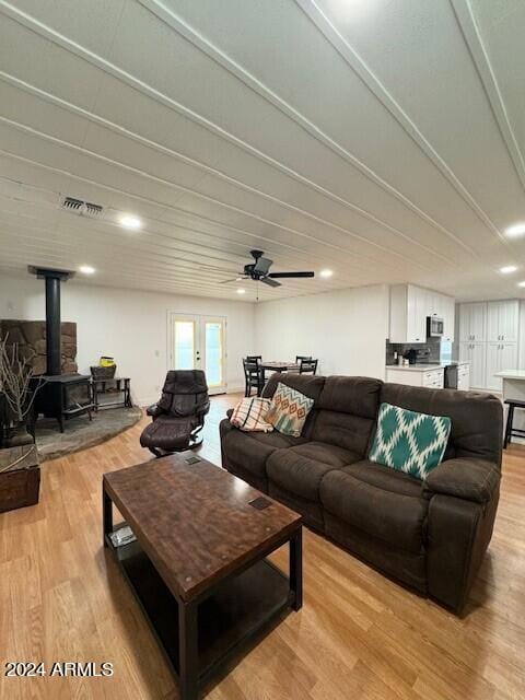 living room featuring french doors, a wood stove, ceiling fan, and light wood-type flooring