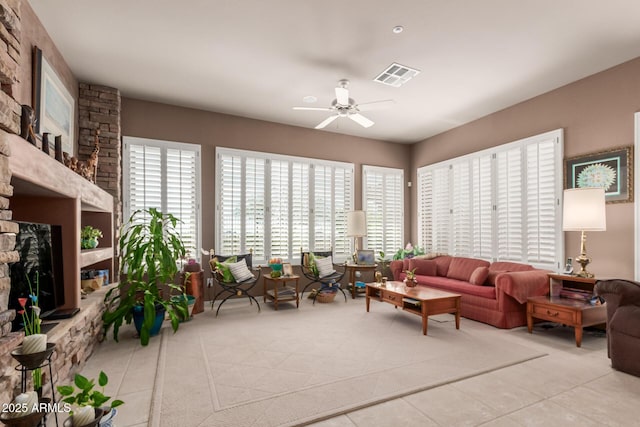 living room featuring ceiling fan, a healthy amount of sunlight, and a stone fireplace