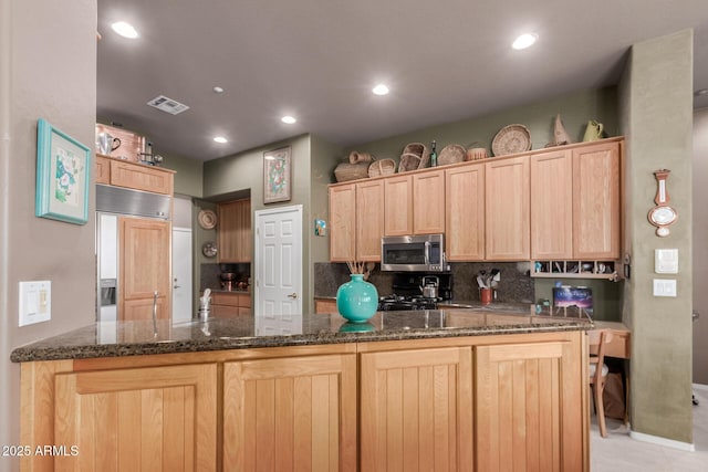 kitchen featuring dark stone countertops, tasteful backsplash, paneled fridge, kitchen peninsula, and light brown cabinets