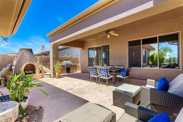view of patio with a ceiling fan, outdoor dining area, a fireplace, fence, and an outdoor kitchen