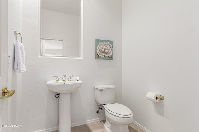 half bathroom featuring baseboards, a sink, and toilet