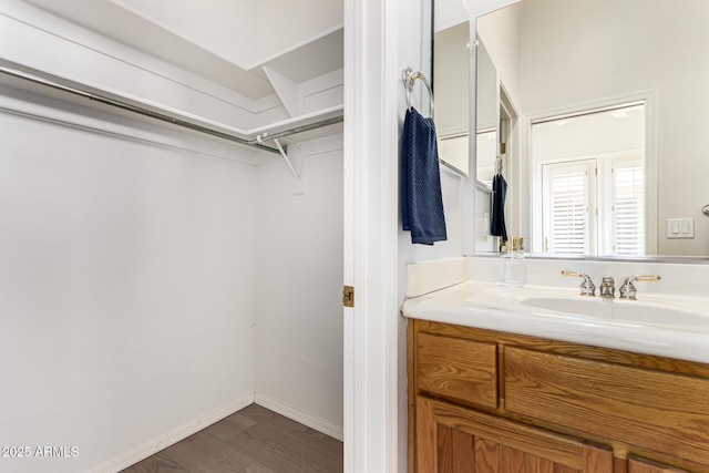 bathroom featuring vanity, baseboards, a walk in closet, and wood finished floors