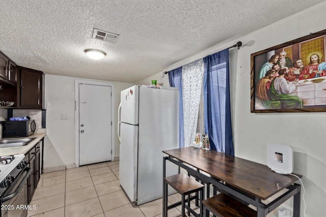 3702 W Sherman St, Phoenix, AZ 85009 - kitchen with freestanding refrigerator, dark brown cabinetry, a textured ceiling, gas stove, and light tile patterned floors