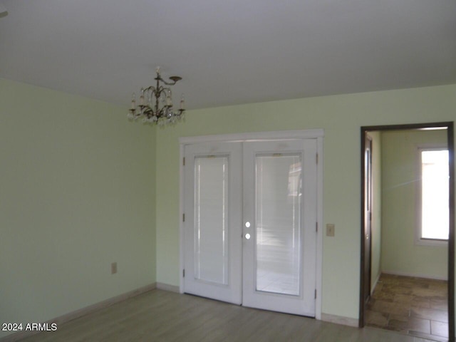 unfurnished bedroom featuring light hardwood / wood-style floors, french doors, and an inviting chandelier