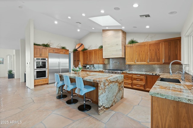 kitchen with wall chimney exhaust hood, appliances with stainless steel finishes, a center island, and light stone counters