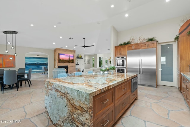 kitchen featuring a spacious island, light stone counters, pendant lighting, stainless steel appliances, and a fireplace