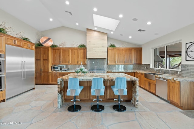 kitchen with a kitchen island, appliances with stainless steel finishes, sink, light stone countertops, and custom range hood