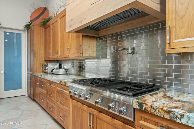 kitchen featuring tasteful backsplash, wall chimney exhaust hood, light stone countertops, and stainless steel gas cooktop