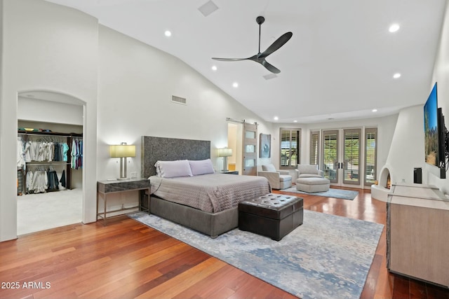 bedroom with ceiling fan, hardwood / wood-style floors, high vaulted ceiling, a barn door, and a closet