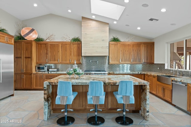 kitchen featuring lofted ceiling with skylight, a breakfast bar, light stone counters, appliances with stainless steel finishes, and a kitchen island