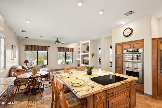 kitchen featuring a kitchen bar, light stone counters, a kitchen island, stainless steel double oven, and black electric stovetop