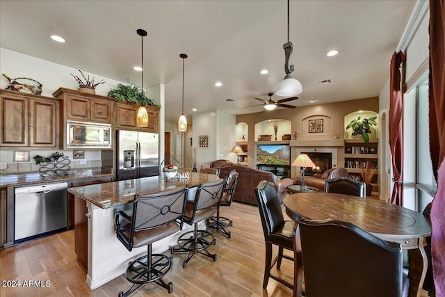 kitchen with ceiling fan, stainless steel appliances, dark stone countertops, light hardwood / wood-style floors, and decorative light fixtures