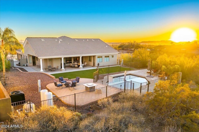 pool at dusk with a patio, an outdoor living space with a fire pit, and a lawn