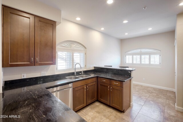 kitchen featuring sink, kitchen peninsula, dark stone counters, light tile patterned floors, and dishwasher