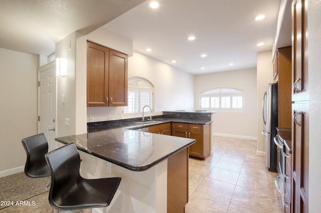 kitchen featuring stainless steel appliances, light tile patterned floors, sink, a breakfast bar, and kitchen peninsula