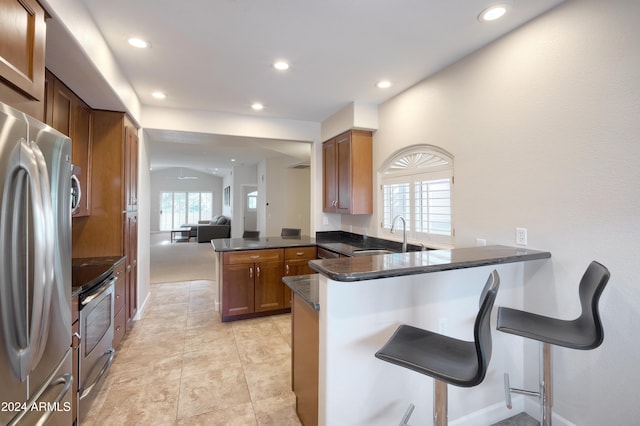 kitchen with kitchen peninsula, sink, a kitchen breakfast bar, appliances with stainless steel finishes, and dark stone countertops