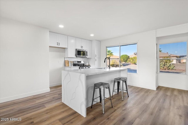 kitchen featuring appliances with stainless steel finishes, a kitchen island with sink, sink, white cabinetry, and a breakfast bar area