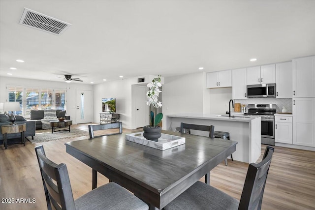 dining room with ceiling fan, sink, and light hardwood / wood-style flooring