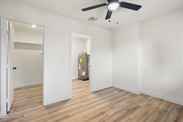 unfurnished bedroom with light wood-type flooring, a walk in closet, ceiling fan, water heater, and a closet