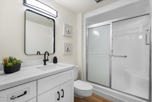 bathroom with hardwood / wood-style floors, vanity, a shower with shower door, and toilet