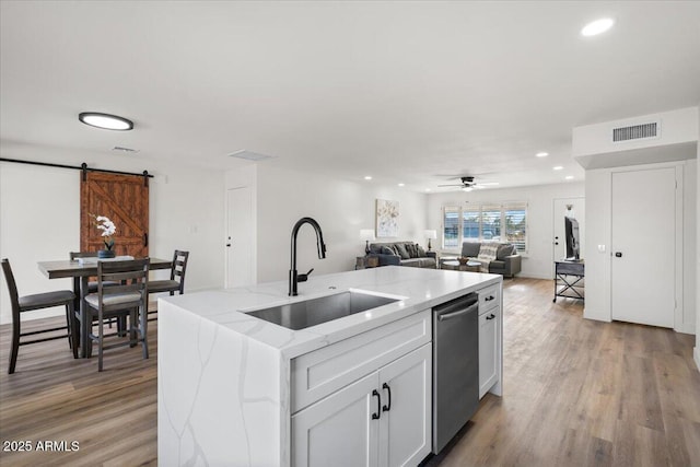 kitchen featuring light stone counters, stainless steel dishwasher, sink, a barn door, and white cabinetry