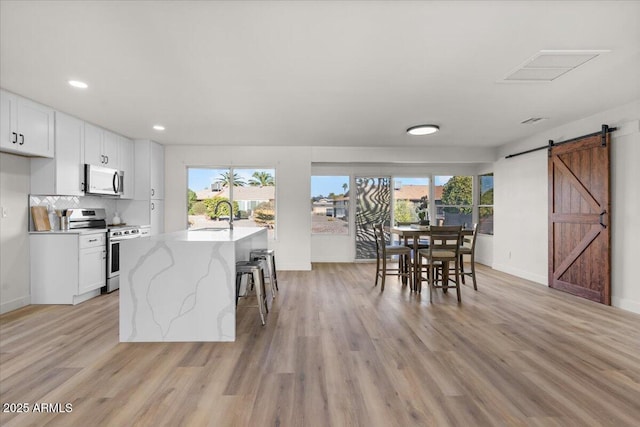 kitchen with stainless steel appliances, a barn door, an island with sink, a kitchen bar, and white cabinets