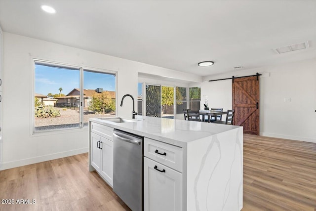 kitchen featuring dishwasher, sink, a barn door, an island with sink, and white cabinetry