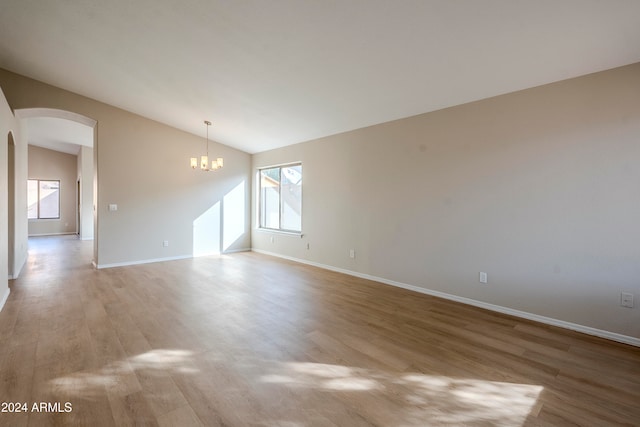 empty room featuring lofted ceiling, light wood-type flooring, and a chandelier