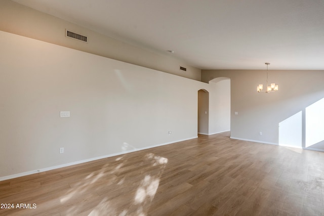 empty room featuring wood-type flooring, an inviting chandelier, and lofted ceiling