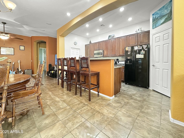 kitchen featuring backsplash, black fridge with ice dispenser, a kitchen island, ceiling fan, and a breakfast bar area