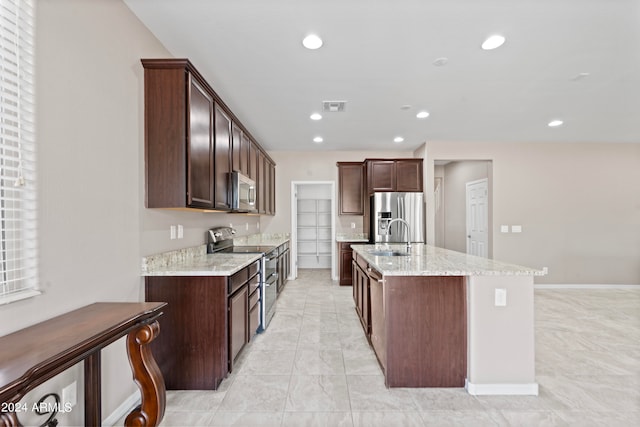 kitchen with light stone counters, stainless steel appliances, dark brown cabinets, a kitchen island with sink, and sink