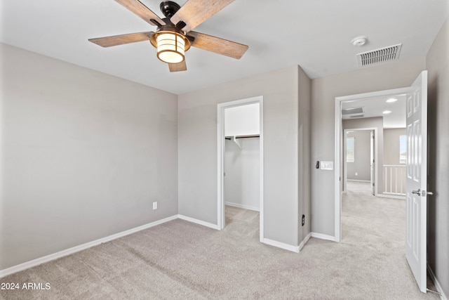 unfurnished bedroom with a spacious closet, a closet, ceiling fan, and light carpet