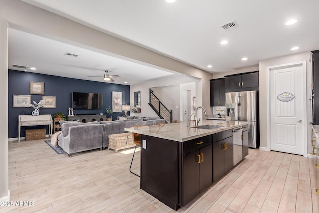 kitchen with appliances with stainless steel finishes, sink, light stone counters, ceiling fan, and a center island with sink