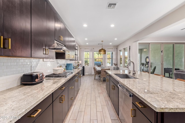 kitchen featuring sink, a center island with sink, appliances with stainless steel finishes, pendant lighting, and decorative backsplash