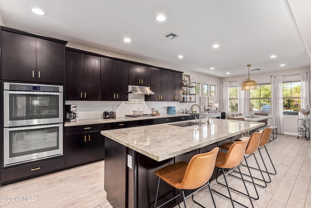 kitchen featuring appliances with stainless steel finishes, decorative light fixtures, an island with sink, sink, and a kitchen bar