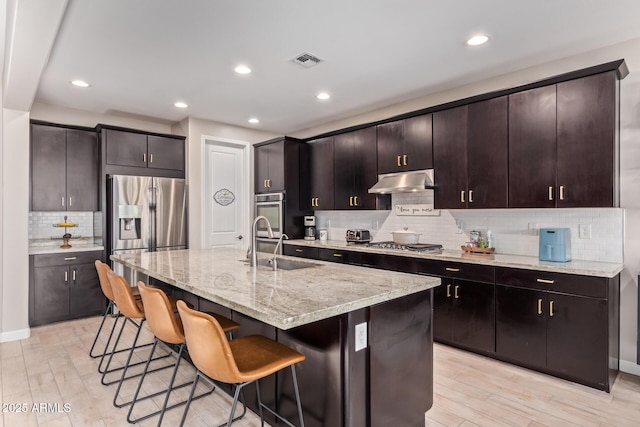 kitchen with light hardwood / wood-style flooring, sink, dark brown cabinets, and an island with sink