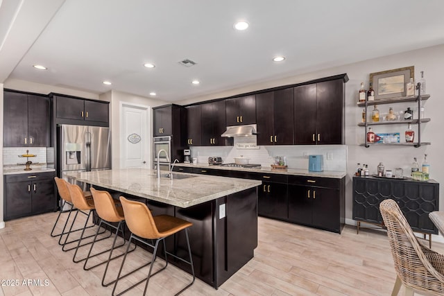 kitchen featuring appliances with stainless steel finishes, an island with sink, sink, a breakfast bar area, and light stone countertops