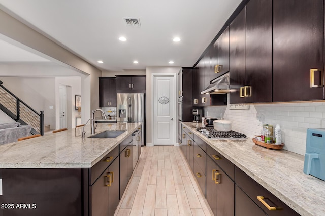 kitchen featuring sink, light stone counters, tasteful backsplash, stainless steel appliances, and a kitchen island with sink