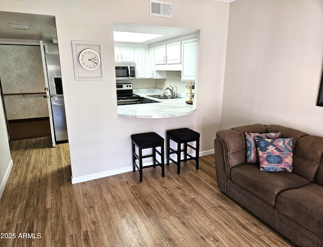 kitchen with white cabinetry, kitchen peninsula, appliances with stainless steel finishes, light wood-type flooring, and sink