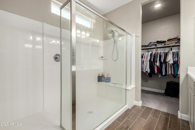 bathroom featuring vanity, baseboards, a walk in closet, wood finish floors, and a shower stall