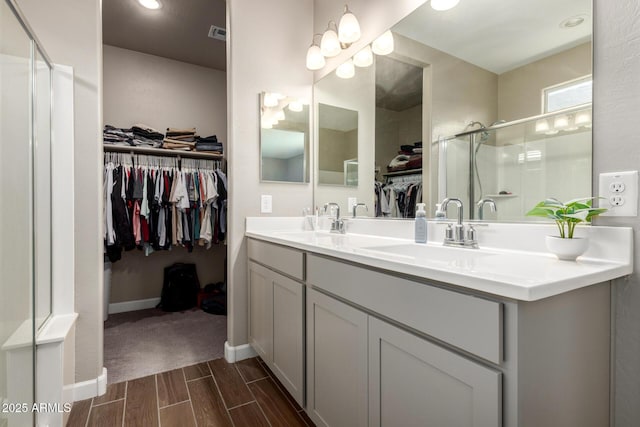 bathroom featuring a sink, a walk in closet, a stall shower, and double vanity