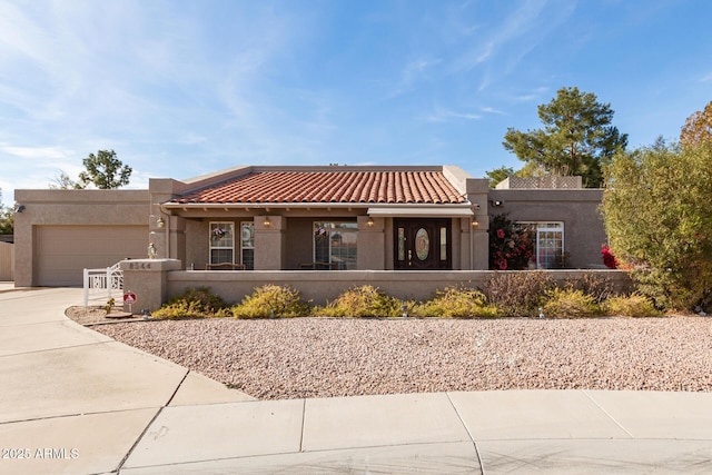 southwest-style home with driveway, a tile roof, an attached garage, and stucco siding