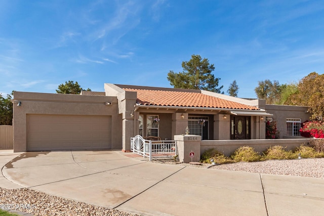 pueblo-style home featuring a garage, driveway, a tiled roof, and stucco siding