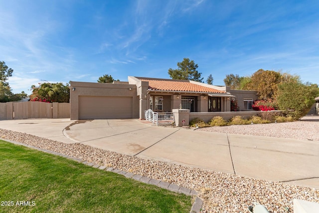 view of front of property featuring a fenced front yard, an attached garage, a tile roof, concrete driveway, and stucco siding