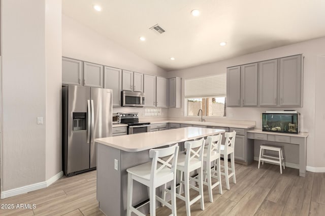 kitchen featuring vaulted ceiling, a kitchen island, appliances with stainless steel finishes, sink, and a breakfast bar area