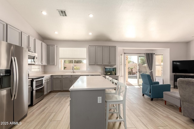 kitchen with sink, gray cabinets, appliances with stainless steel finishes, a center island, and a kitchen bar