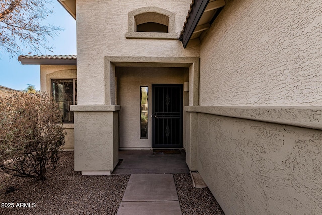 view of exterior entry with a tiled roof and stucco siding